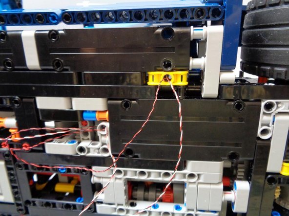 Back under the car, carefully thread BOTH cables through the hole in the YELLOW Technic bracket and up toward the top of the car as shown in the second photo.