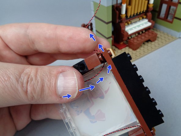As shown by the blue arrows in the second photo for this step, lift the top section of the painting frame slightly, just enough to pass the LED light wire through and out the side of the frame.