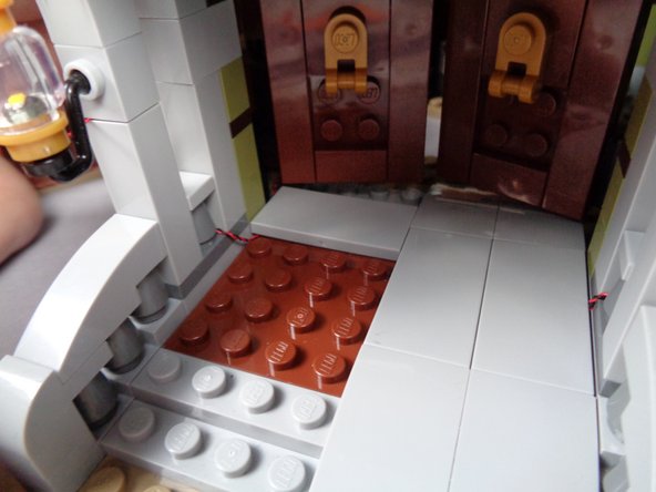 As shown in the first photo for this step, carefully replace the 2x4 LEGO tile on the porch floor, making sure the light wire continues as close to the wall as possible so as not to be pinched passing on top of any studs.