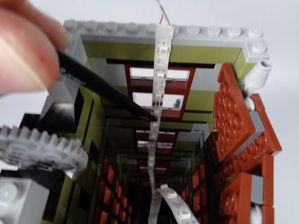 As shown in the third photo for this step, align the first light strip so it continues upward in a straight line from the lower section.  The photo shows the tweezers being used to help place the light strip.