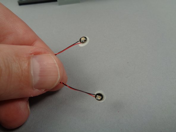 As shown in the second and third photos for this step, take two small sticky discs and attach them to the back of the two green LED lights.