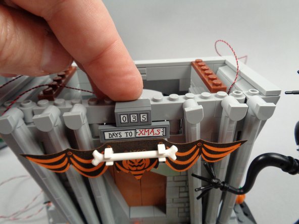 As shown in the third photo for this step, re-attach the town hall sign, making sure not to pinch the LED light wire for the banner light.