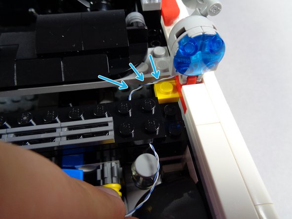 As shown by the green arrows in the second photo for this step, run the light wire between the studs of the long black brick and into the engine area.