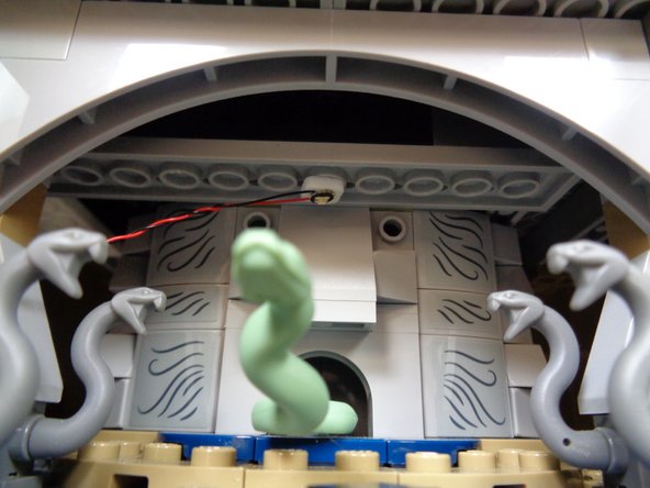 As shown in the second and third photos, use one of the small sticky squares in Bag 1 to attach the green light to the area in the Chamber of Secrets above the snake.