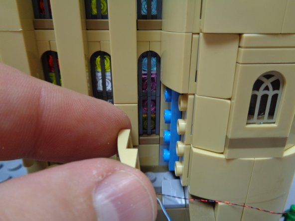 As sown in the second and third photos, remove the tan slope pieces that run up the side of the tower on the right side of the castle, then remove the light blue plates under the tan slopes.