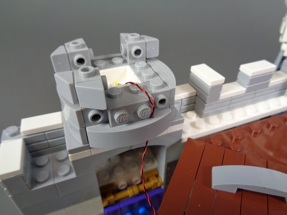 As shown in the photos for this step, carefully re-assemble the first tower, making sure the LED light wire runs between, not on top of, any studs.