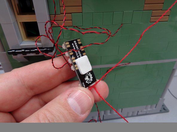As shown in the first photo, use one of the large sticky squares from Bag 1 to attach the BRANCH09X adapter board to the back of the house.