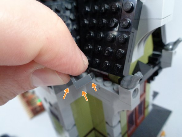 As shown by the orange arrows in the first photo for this step, and also by the orange rectangle in the second photo, re-attach the dark bluish gray panel piece along the edge of the roofline.