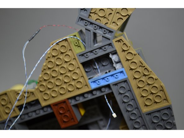 As shown in the photos for this step, carefully feed the boathouse wires through the holes in the Technic bricks at the base of the castle.  The plugs are small enough that they will fit through the holes.
