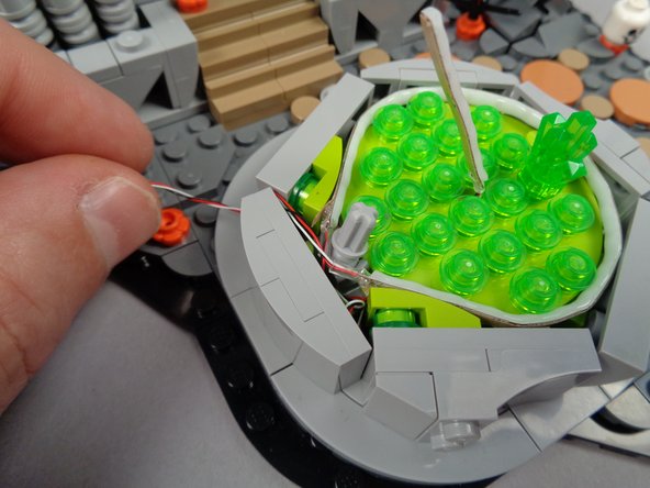 As shown in the second photo for this step, tuck any excess wire into the base of the fountain and pass the long LED strip wire through the gap in parts at the back of the fountain.