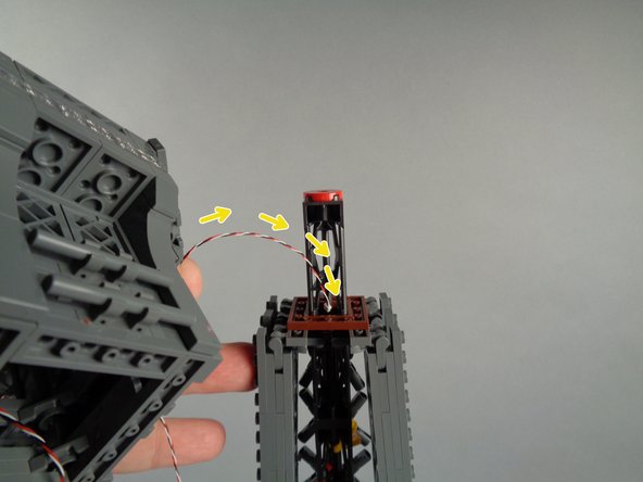 As shown by the yellow arrows in the first photo for this step, pass the control cable for the broadcast tower down through the center of the tower top, inside of the brown square plate.