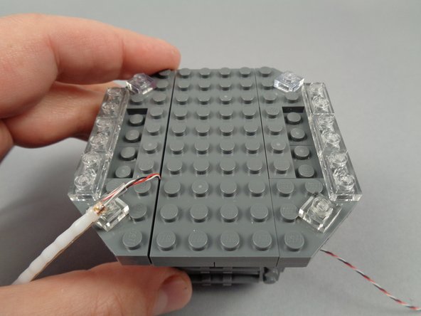 As shown by the third photo for this step, re-attach the center section of the broadcast tower, holding the wire in place for the flexible LED light strip.