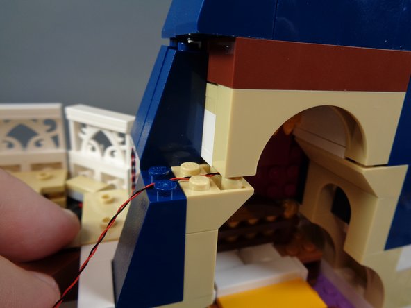 As shown in the photos for this step, remove the blue roof slope piece next to the bedroom, carefully lift the arch section, and pass the bedroom light wire through, making sure to run the wire between, not on top of, studs.