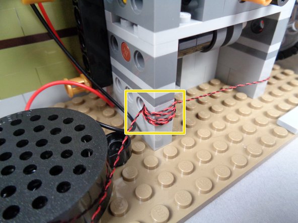 As shown by the yellow rectangle in the third photo for this step, feed the lamp LED Light wire through the holes in the Technic brick and wrap the wire several times to hold it in place.  Make sure to keep the wires away from any gears.