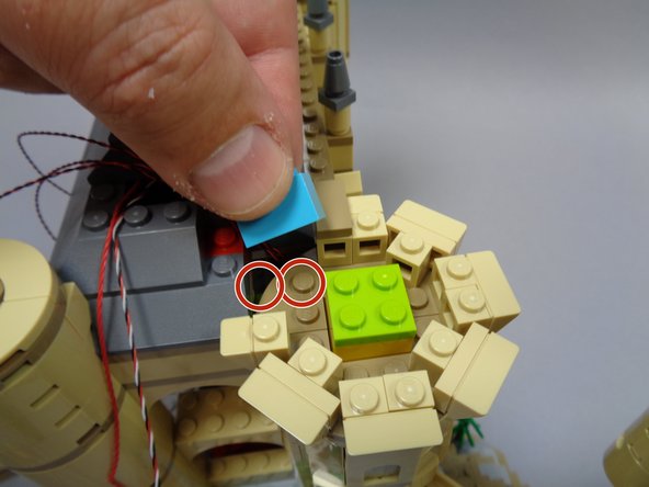 As shown by the two red circles in the second photo, attach the light blue 1x2 brick you removed from under the roof earlier.  Note that the brick will attach to only one stud underneath.