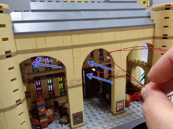 As shown by the blue arrows in the first photo, run the two fireplace light wires up and under the ceiling area of the common room.