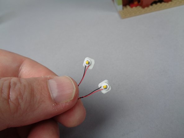 As shown in the second photo for this step, place two sticky squares on the back side of the two white Pico LED lights.