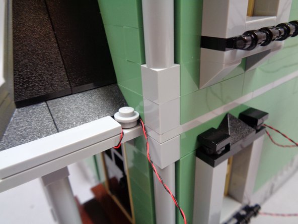As shown in the third photo, use the round 1x1 LEGO® plate on the side porch roof to hold the light wire in place.