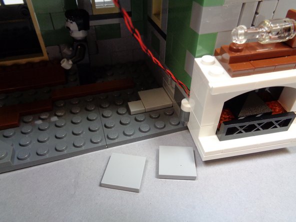 As shown in the first photo, remove the two large 2x2 LEGO® tiles behind the fireplace.
