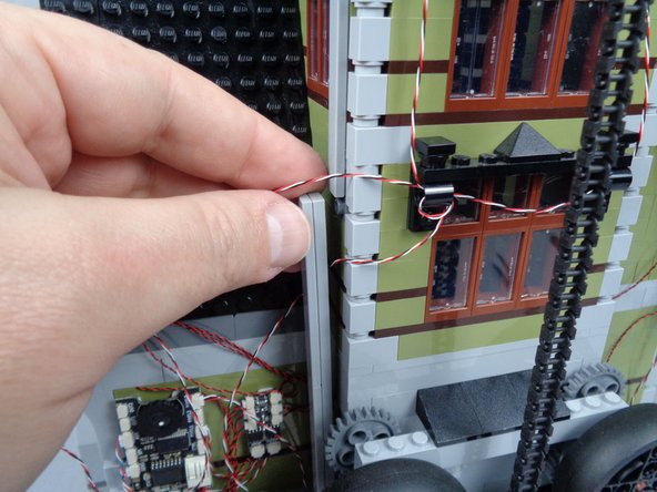 As shown in the photos for this step, finish routing the light strip wire by passing it behind the long LEGO tile used to support the tower.  The tile should hold both the light strip wire and the magnetic switch wire in place.