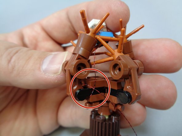 As shown in the first photo, position the car back in the tree branches and wind the light power wire around the branches several times to hold the car in place as shown by the red circle.