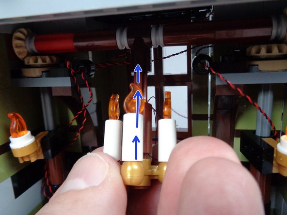 As shown by the blue arrows in the first photo for this step, carefully re-attach the chandelier by sliding its brown axle back into the black Technic connector part mounted on the top axle that moves the front doors.