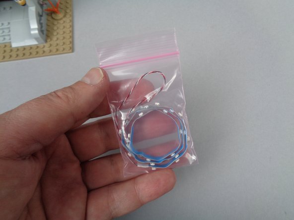 As shown in the photos for this step, take one of the light strips out of its bag and carefully remove the adhesive backing from the entire length of the strip.