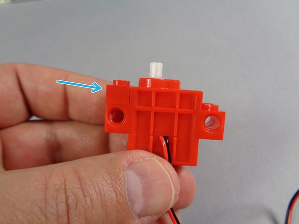 As shown by the blue arrow in the first photo for this step, attach the two 1x2 red plates to the end of the motor closest to the white axle.