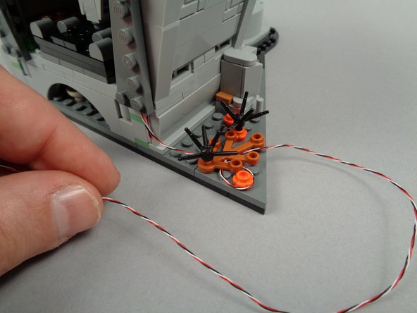 As shown by the two photos for this step, you can route the control wire to the edge of the town hall section base by passing it beneath the brown leaf and orange flower plate parts to hold it in place.