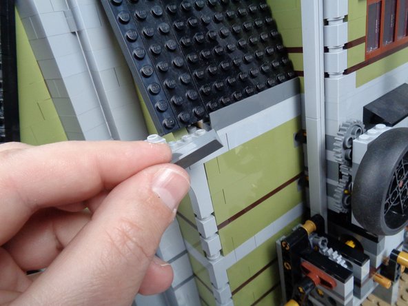 As shown in the second photo for this step, remove one of the dark bluish gray panel pieces from the left back side of the mansion roof.