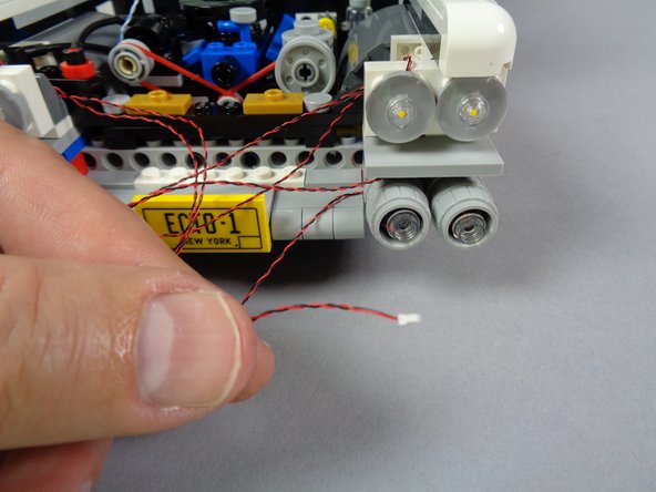 As shown in the second photo for this step, re-attach the second lower headlight after you have mounted the LED light, with the light wire passing to the top and toward the center of the Ecto-1.