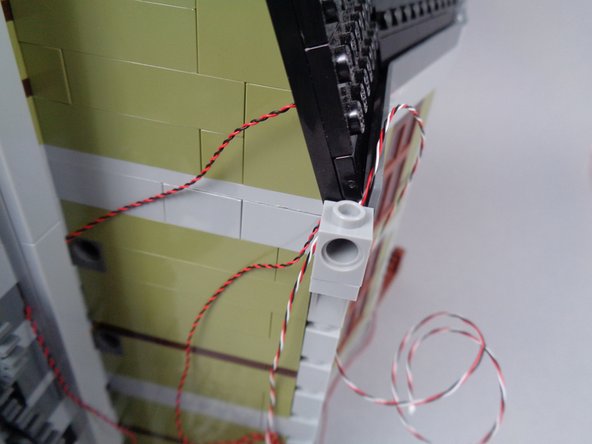 As shown in the photos for this step, run the 3-wire cable up to the roof of the mansion and use the 1x1 Technic brick to hold it in place.