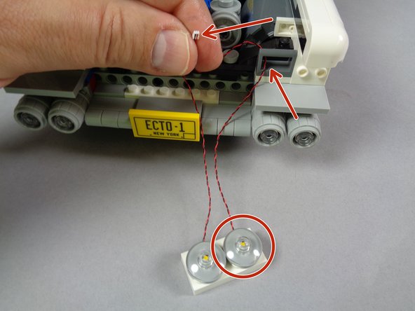As shown in the first photo, take the light wire from the rightmost headlight on the first assembly, pass it through the dark bluish gray bracket (red arrow), and pull it through.