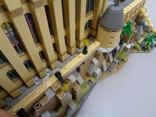 As shown in the three photos for this step, carefully mount the pre-wired lamp post string.  It is ok to press down on the wires as you mount the lamp posts.