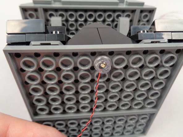 As shown in the two photos for this step, press the yellow LED light and round transparent plate into the center antistud in the first row facing the front of Jack's house.