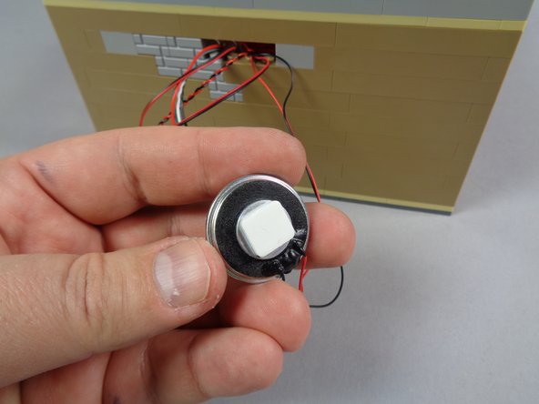 As shown in the second and third photos, you can use one of the large sticky squares included with your kit to mount the video player speaker to the outer cinema wall.