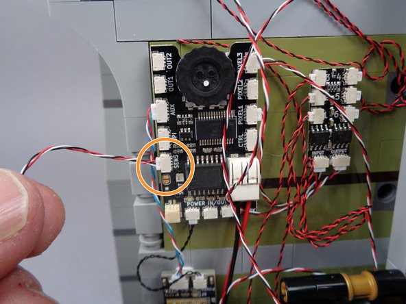 As shown by the orange arrow and circle in the photos for this step, connect the magnetic switch wire to the plug labeled &quot;SENS&quot; on the main effect controller.