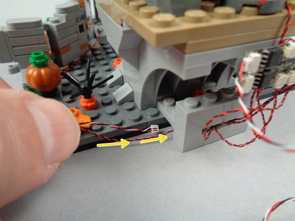 As shown by the yellow arrows in the first and second photos for this step, route the 3-wire connecting cable plugged into the INPUT of the BRANCH06X driver board underneath the wire base you built and out toward the tree.