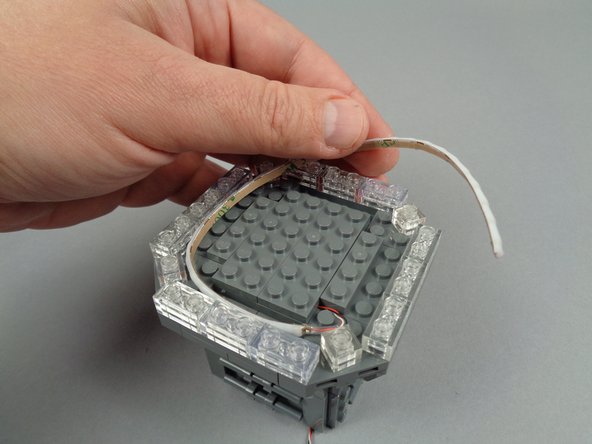 As shown in the photos for this step, take the flexible LED light strip and wrap it around the channel in the broadcast tower, behind the clear plates.