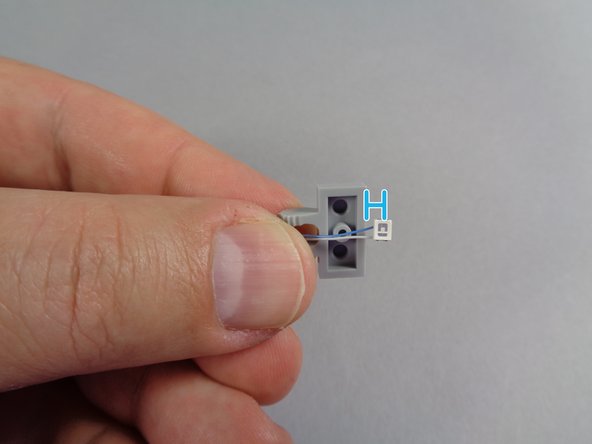 As shown in the second photo for this step, carefully place one of the blue LED lights with longer wires on the 1x2 plate, on the side opposite the studs.
