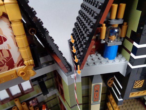 As shown by the orange arrows in the first photo for this step, continue running the 3-wire cable along the roof line behind the dark bluish gray panels.