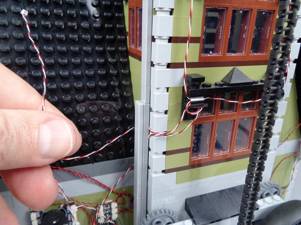 As shown in the photos for this step, finish routing the light strip wire by passing it behind the long LEGO tile used to support the tower.  The tile should hold both the light strip wire and the magnetic switch wire in place.