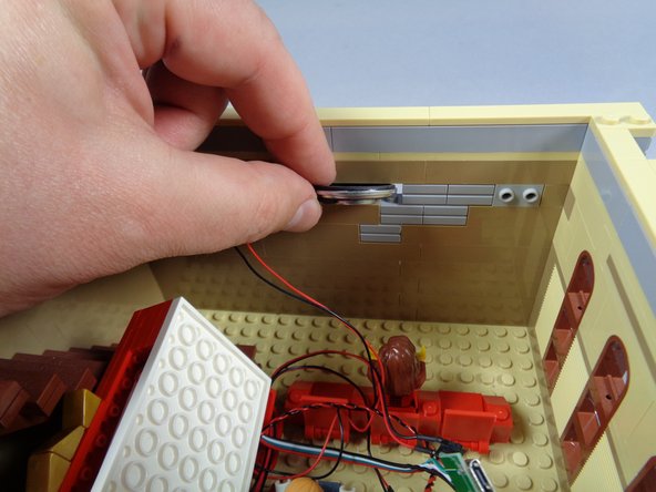 As shown by the two photos in this step, next you will pass the video player wires through the hole in the wall that you made earlier by removing the two light bluish gray bricks.