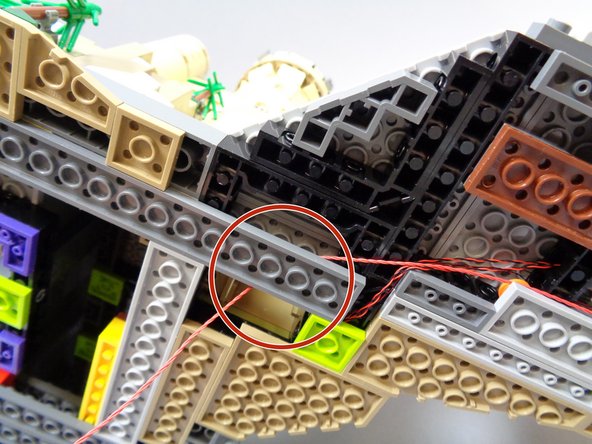 As shown by the red circle in the second photo, run the red wire beneath the long dark bluish gray plate under the castle.