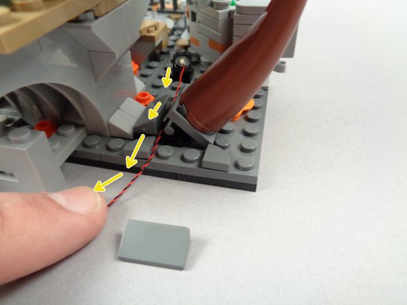 As shown by the yellow arrows in the second photo for this step, remove the 1x2 slope behind the tree and run the green LED light wire toward the back, using the hinge of the tree to hold the wire in place.