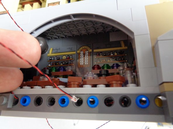 As shown in the first photo, feed the power wire from the cauldron light through the hole in the Technic brick just below the front of the Potions Class.