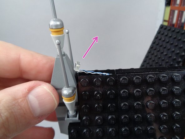 Re-attach the front pyramid roof piece as shown in the first photo for this step.  As shown by the purple arrow, make sure the lightning LED light is pointed at an angle back toward the mansion.