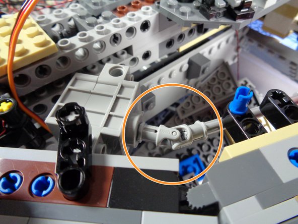 As shown by the red circle in the first photo, attach one end of the long light bluish gray axle to the end of the black axle using the universal joint.
