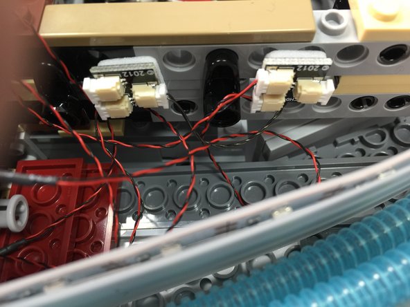 As shown in the third photo, carefully pass the two 6&quot; connecting cable wire ends through the frame in the gap between the two long Technic bricks.