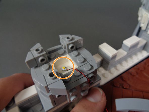 As shown by the orange circle in the third photo, stick the LED light in the center of the tower so it is pointing upward, and so its wire runs toward the back of the castle.